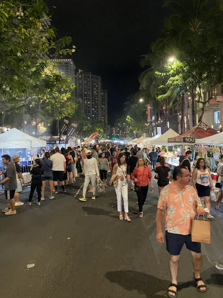 Night market on Kalakaua Avenue in Honolulu with food stalls, lights, and people walking around