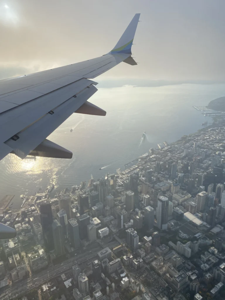 View of Seattle from the airplane window while flying toward Hawaii, with city skyline and water below